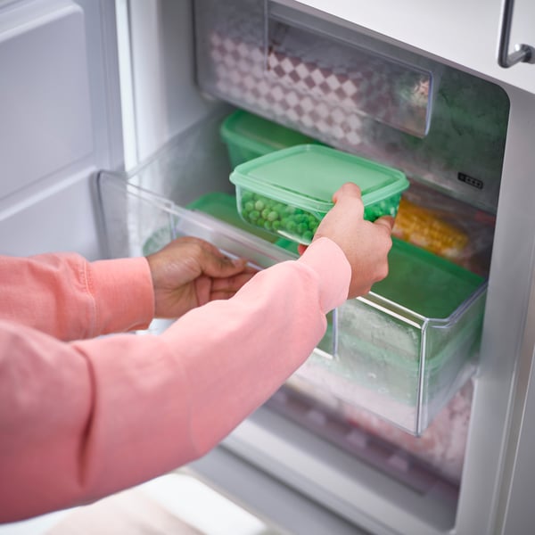 Person som öppnar ett kylskåp för att komma åt förvaringsbehållare av plast i olika storlekar som används för att lagra rester och spara utrymme under lagring.