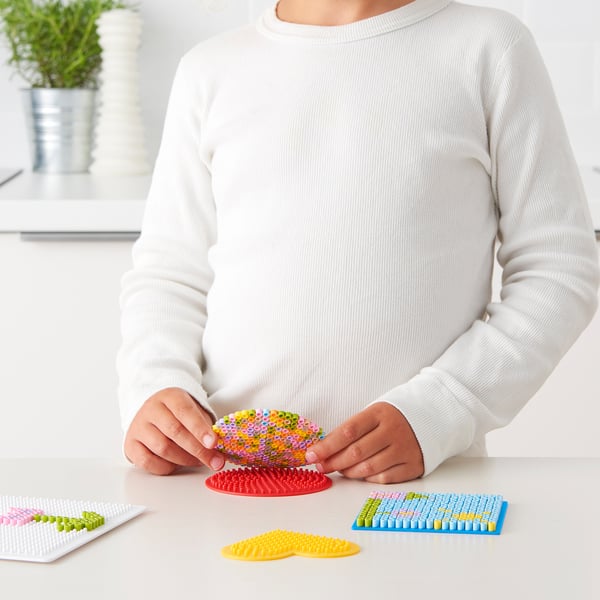 Ett barn som arrangerar färgglada pärlor på en röd plastbas och lär sig finmotorik samtidigt som de skapar konst.