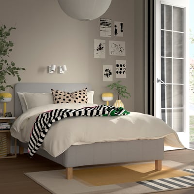 Modernt beige sovrum med sängen RÅHOLMAR , randig kudde, svartvit filt, gul lampa, växter och abstrakt konst.