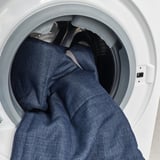 Inuti en vit tvättmaskin syns ett mörkt plagg, vilket indikerar maskinens kapacitet att hantera stora laster.