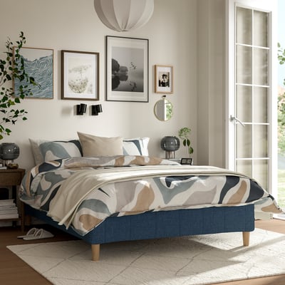 Modernt sovrum med RÅHOLMAR-säng, blå, abstrakt mönstrat sängkläder, träben, inramad konst, grönska, stilren lampa, ren design och naturligt ljus.