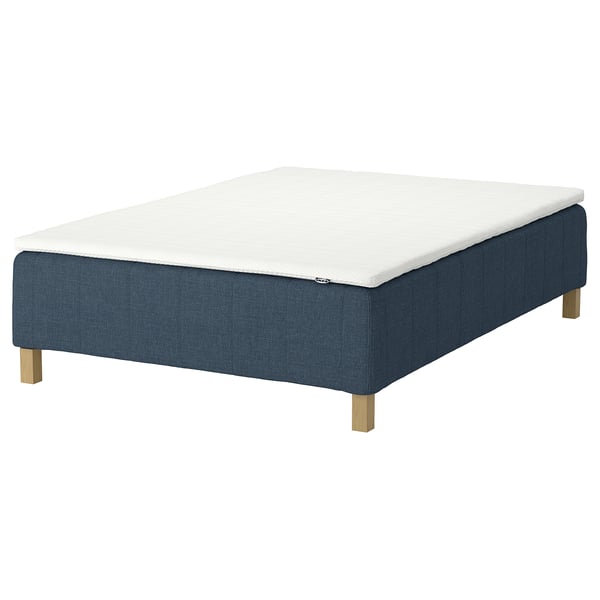 En blå sängbotten från IKEA RÅHOLMAR med vit madrass. Det är en elegant design med träben.