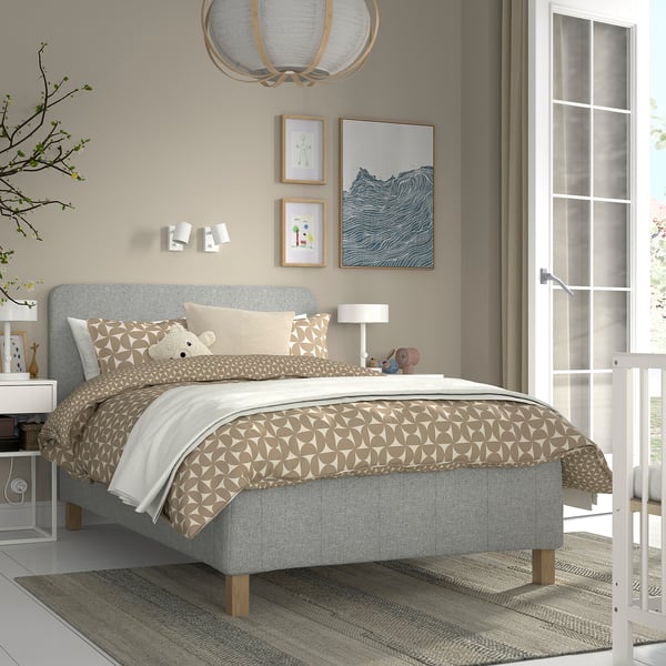 Modernt sovrum med grå säng RÅHOLMAR , mönstrade sängkläder, vitt nattduksbord, beige väggar, naturligt ljus från fransk dörr och stilren taklampa.