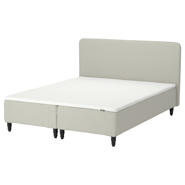 Sängen RENFJÄLLET i ljusbeige, klädd med tyg, med en mjuk sänggavel och mörka träben.