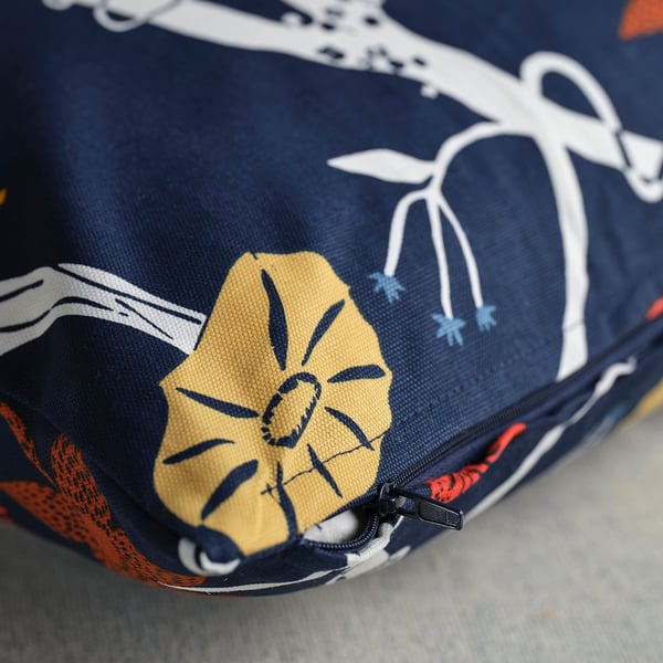 Närbild på ett livfullt, detaljerat kuddfodral med en gul blomma och botanisk design på mörkblått tyg.