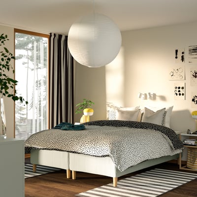 Modernt sovrum med stilren säng, pendellampa, konstverk och fönsterutsikt.