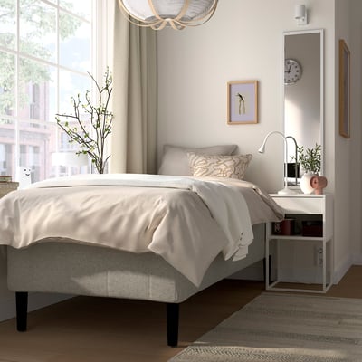 Modernt sovrum med sängen RISHÖJDEN , neutrala sängkläder, stort fönster, nattduksbord, minimalistisk inredning, klocka, konst, spegel, växt, pendellampa.