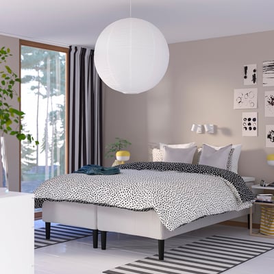 Modern sovrum med RISHÖJDEN-säng , pendellampa, mönstrat täcke, randig matta, mörka gardiner, konst, stort fönster, växt.