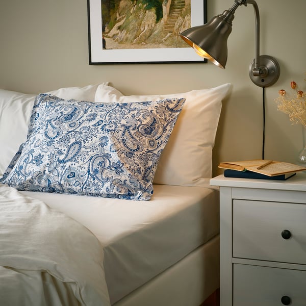 Sovrum med RODGERSIA paisley örngott, beige sängkläder, böcker, torkade blommor, varm lampa.