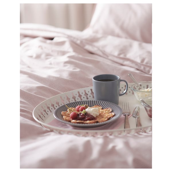 Bricka med frukostartiklar, blå mugg och bestick på rosa sängkläder. Blå tallrik med pannkakor, bär och grädde.