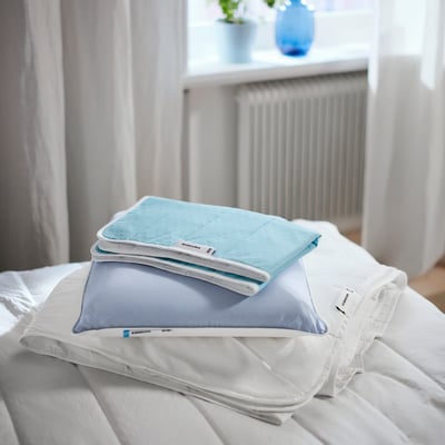 En snyggt bäddad säng med vita lakan och ljusblå sängtillbehör, inklusive ett madrasskydd, örngott och hopvikt täcke.