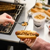 En hand lägger lök från ROSTAD LÖK i en korv i köket.