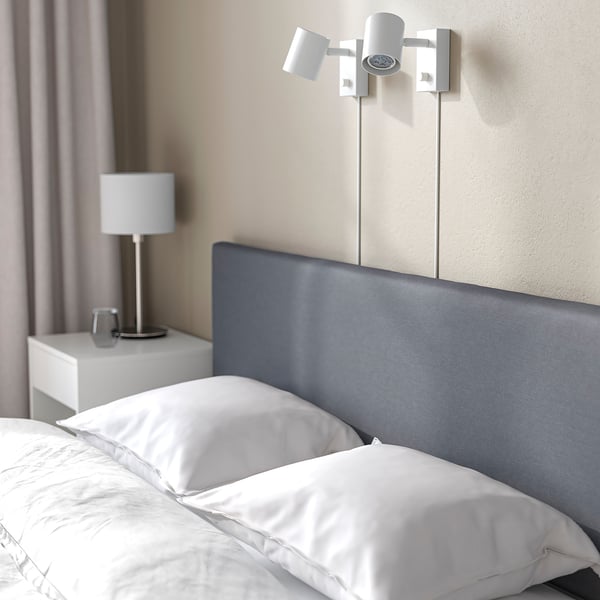 Modern säng med vadderad sänggavel, läslampa, lampa på nattduksbordet.