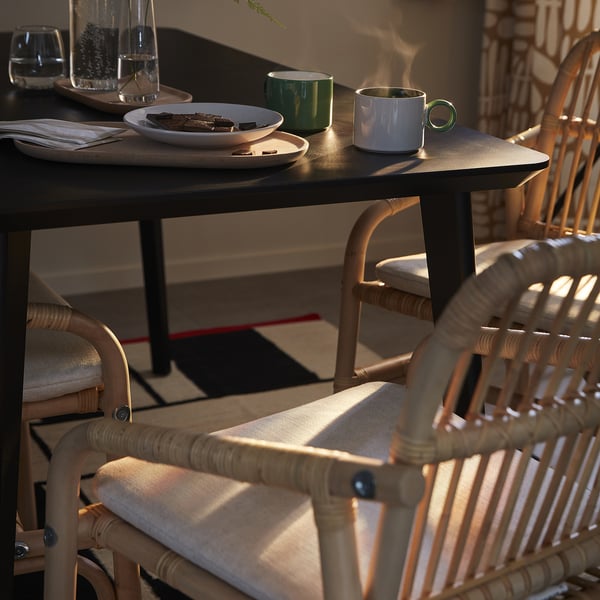 Mysig matuppställning med stolen SALNÖ i ljus rotting bredvid bordet med muggar, tallrikar och glas.