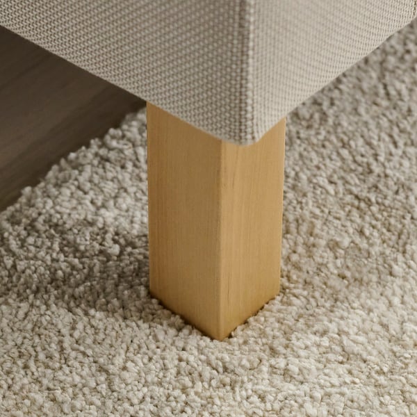 Ett soffben sedd i vinkel, som visar dess robusta byggnad och gyllene yta, vilande på en texturerad off-white matta.