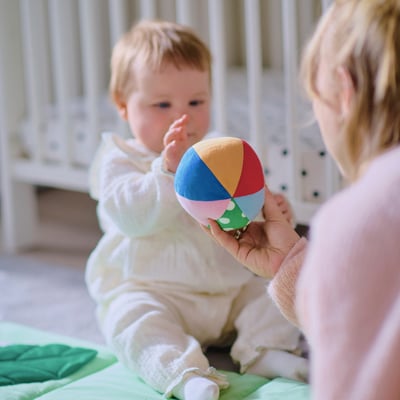 Bebis som håller mångfärgad boll med vuxen, som troligen leker och utvecklar sensoriska färdigheter.