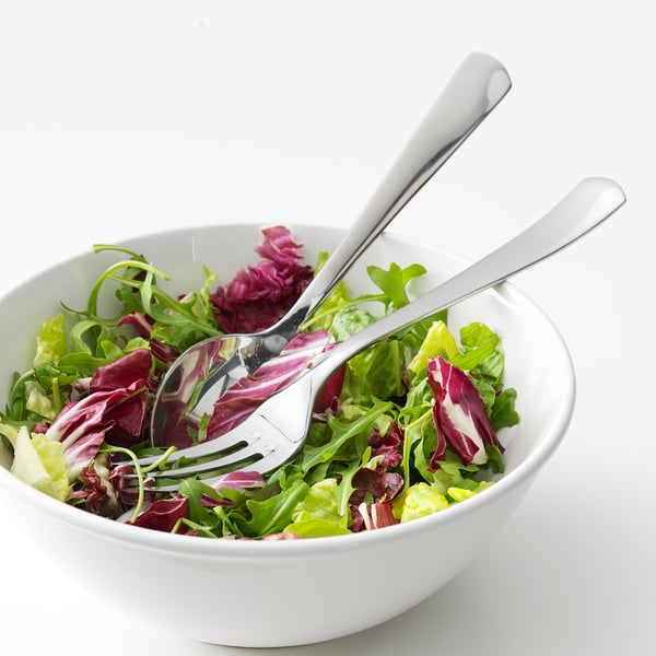 Skål med färsk grönsallad med serveringsredskap i silver.