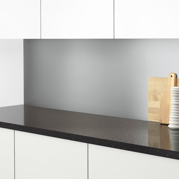 Modern köksbänk med elegant svartspräcklig yta, ljusgrå stänkskydd, träredskap.