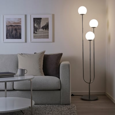 Modernt vardagsrum med grå soffa, soffbord, inramade foton och hög kromad golvlampa med glasglober som lyser upp utrymmet.