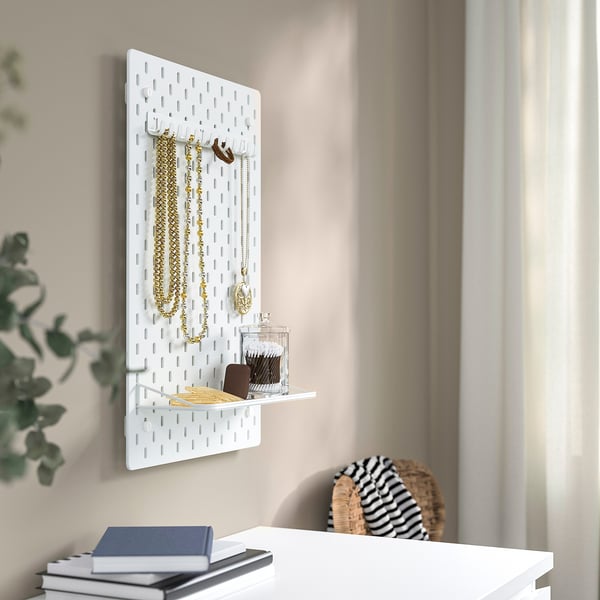 Vägghängd SKÅDIS organizer med krokar och hylla med halsband, hängen och en burk.