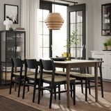 Modernt utdragbart bordsset, vävda stolar, snygg matta, taklampa, hyllor med växter och böcker.