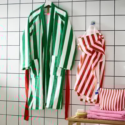 Färgglada handdukar på krokar, gröna/vita, röda/vita ränder bredvid den vikta stapeln.