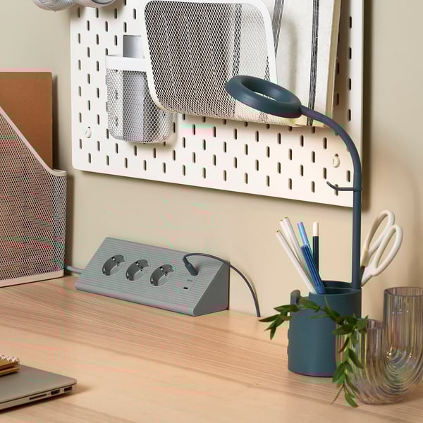 Skrivbordsinstallation med SKOTAT förlängningssladd, bärbar dator, pennhållare, sax och lampa med flera uttag och usb-portar.