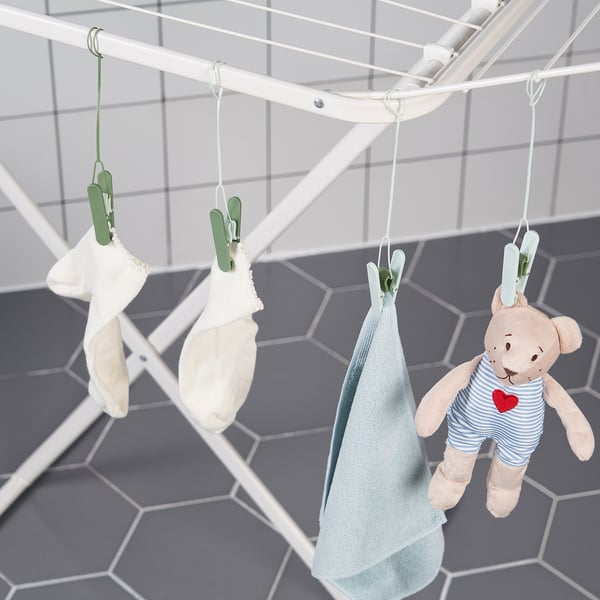 Klädnypor hänger kläder på torkställningar, inklusive babyartiklar och en nallebjörn.