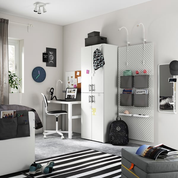 Modernt tonårssovrum med vit SMÅSTAD garderob, skrivbord, grå soffa, randig matta, väggklocka och svarta tillbehör.