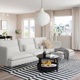 Ett modernt vardagsrum med en vit SÖDERHAMN-soffa och svart soffbord på en randig matta, med stora fönster och naturligt ljus.