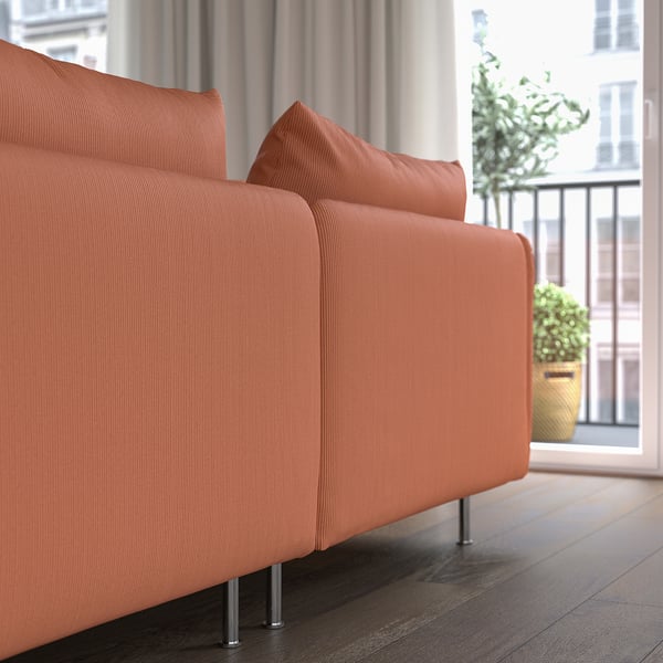 Orange modern soffa vid fönster med växter, som erbjuder komfort och stöd med djupa säten och mjuka kuddar.