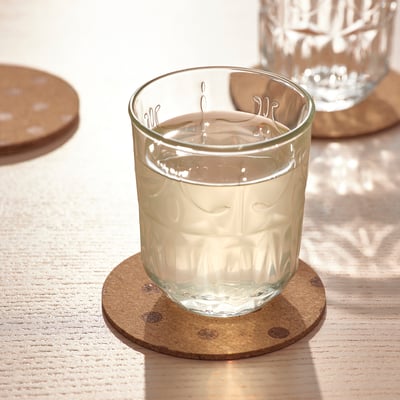 Ett glas fyllt med vatten på ett runt korkunderlägg på ett träbord.