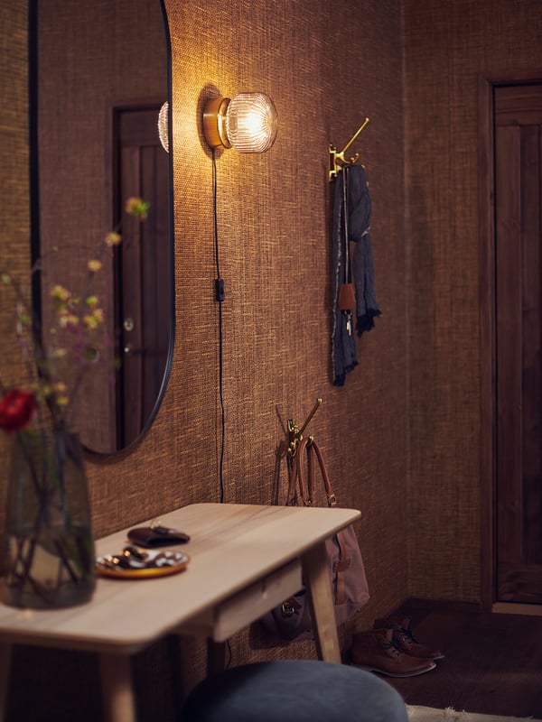 Entré med mässingslampor, texturerad tapet, bänk, nycklar, blommor, spegel.