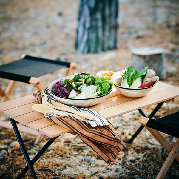 Träskålar med färgglada grönsaker på bambubordet, randiga servetter, svarta/trästolar utomhus.