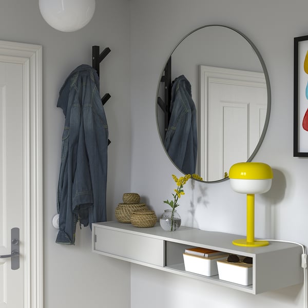 Modern entré med grå vägg, hylla har jeansjacka, lampa, blommor, spegel och förvaring.