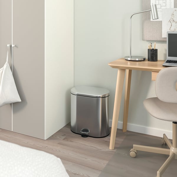 Elegant STABBEN-papperskorg i rostfritt stål i modern kontorsmiljö bredvid ett skrivbord i ljust trä med bärbar dator och lampa.