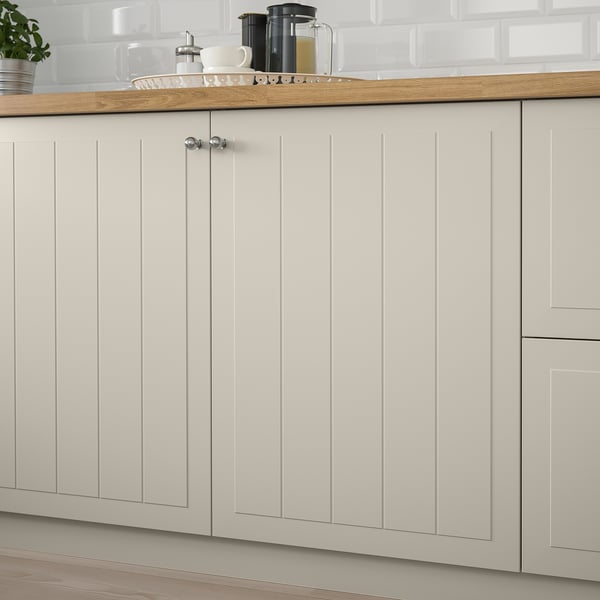 Köksluckor med beige träpaneler, med räfflad design. På bänkskivan finns kaffebryggare och koppar.