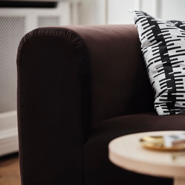 Mörkbrun sammetssoffa med vadderade kuddar och svart/vitrandig kudde som visar upp material och design av hög kvalitet.