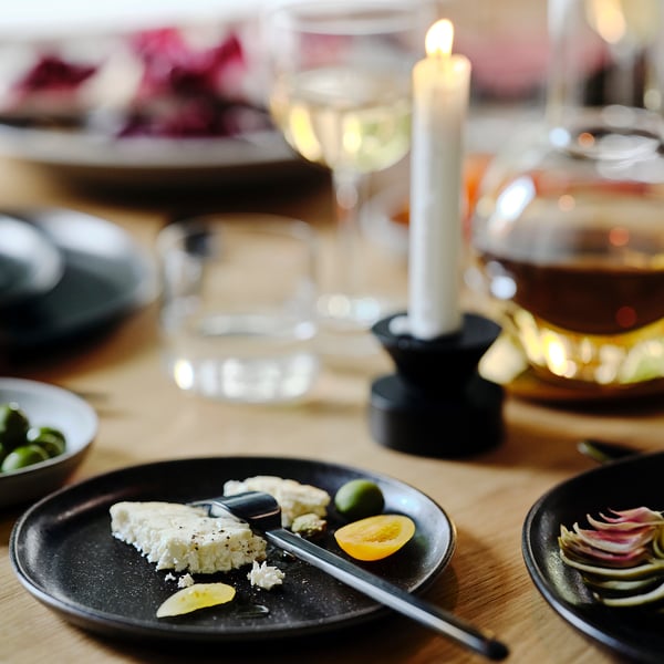 Mörk tallrik med ost, citron, oliver; ljus, glas, skål bredvid.