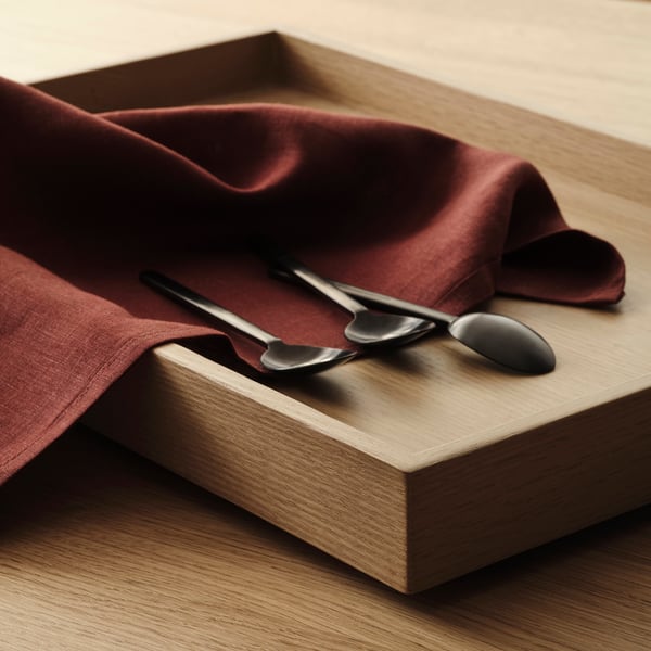 Lyxig röd linneservett har elegant textur och lyster, vikt på träytan med eleganta metallskedar.