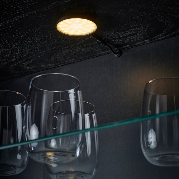 Tre tomma vinglas hänger upp och ner från en mörk trähylla som belyses av en svag, inbyggd spotlight.