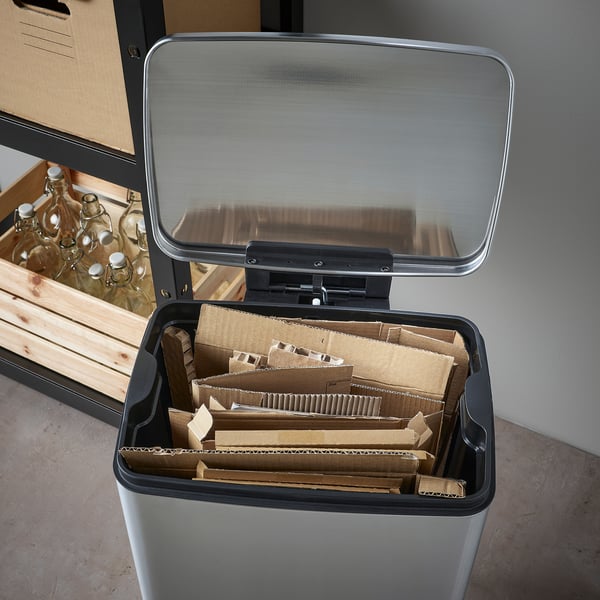 Silverfärgad pedalbehållare med kartongavfall; Locket öppnas och avslöjar interiören fylld med tillplattade kartonger.