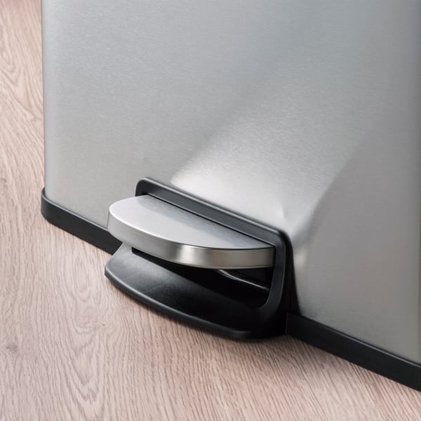 Silverfärgad pedalhink i rostfritt stål med mjukstängande lock och svart bas på trägolv. Högkvalitativ, praktisk design.