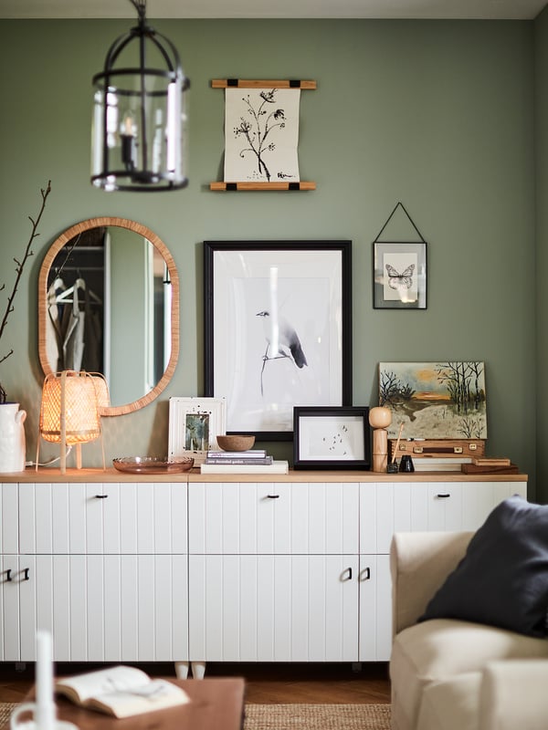Modernt vardagsrum med vitt SUTTERVIKEN sideboard mot grön vägg, dekorerat med konst, spegel och lampa.