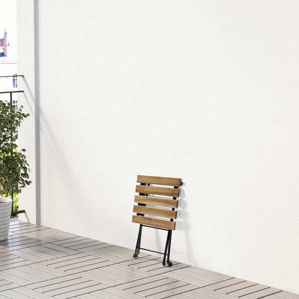 Hopfälld träpall med hjul, lutad mot en vit vägg utomhus.