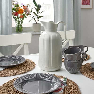 Dukning med grå tallrikar och muggar, vit kanna, sjögrästabletter, blommor och krukväxter.