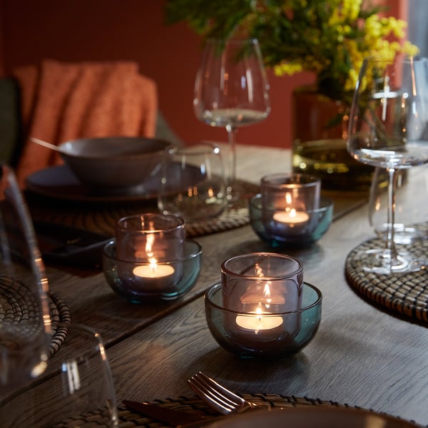 Elegant matbord med tända värmeljushållare, vinglas, bestick och blommor som skapar en varm och inbjudande atmosfär.