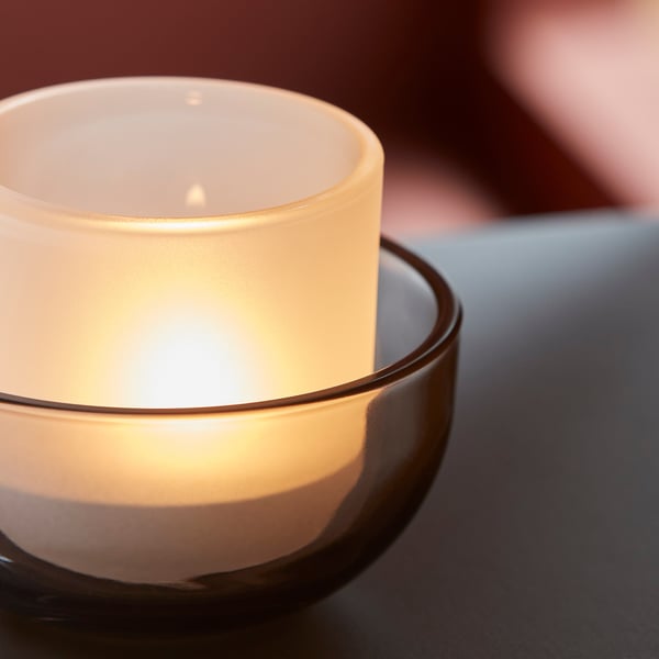 Hög värmeljushållare i glas som avger varmt ljus, placerad på en mörk yta.