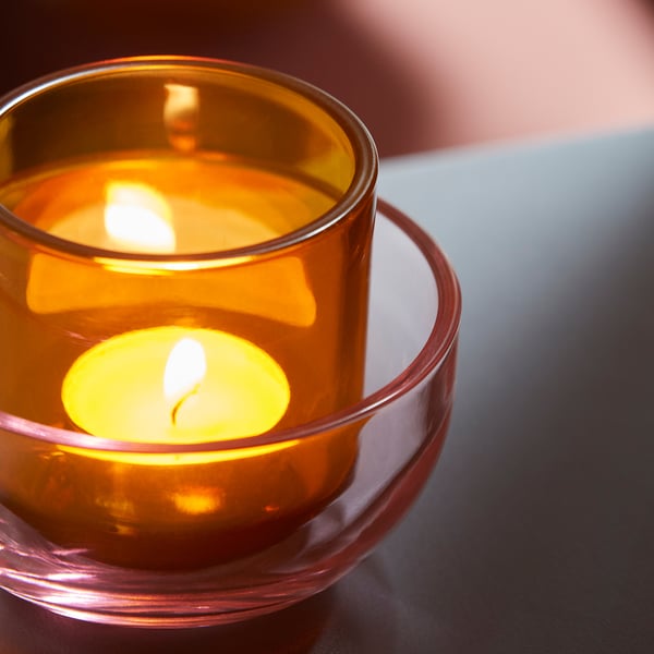 Två värmeljushållare i belyst glas, kapslat, avger varmt bärnstensfärgat ljus. Den ena sitter inuti den andra och skapar en mysig, dekorativ atmosfär.