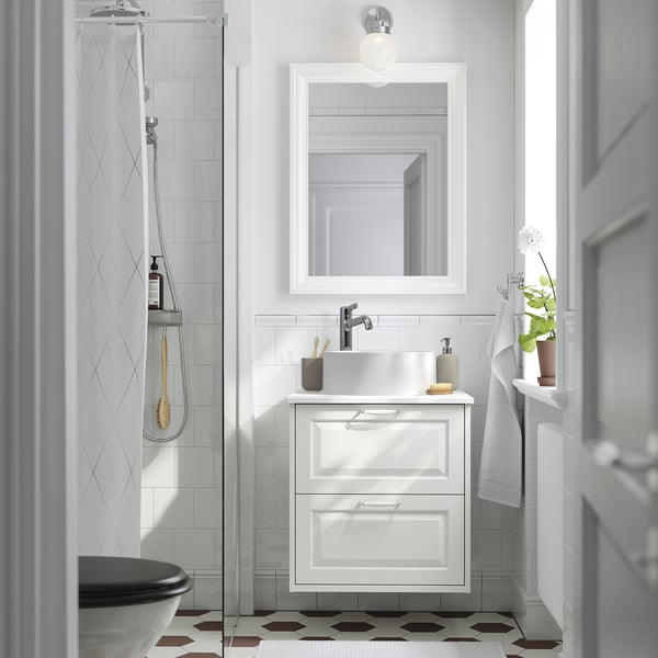 Modernt vitt badrum: hex klinkergolv, handfat i marmor, hängande handdukar, dusch i glas, spegel, enkel glödlampa.